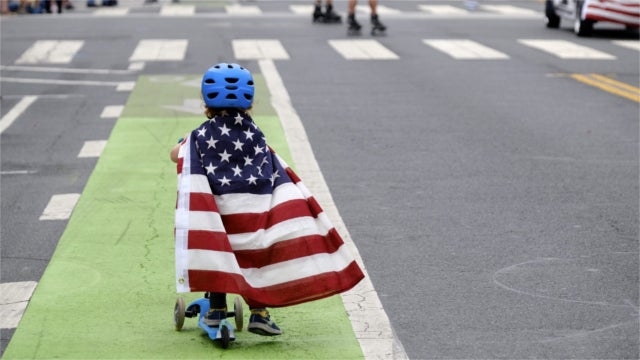 Child on a scooter wearing an American flag as a cape