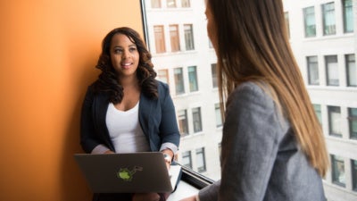 Woman Wearing Gray Blazer Facing Woman Wearing White Shirt and Black Blazer With Laptop on Lap