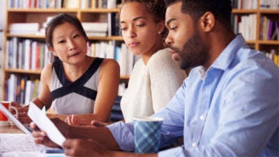 Three people in a library reading a piece of paper.