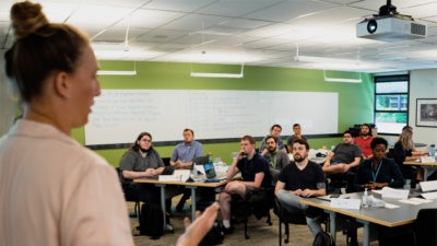 A woman stands at the front of a classroom as she speaks to around a dozen individuals who are seated across the room. Photo credit: Jordan Stead / Amazon