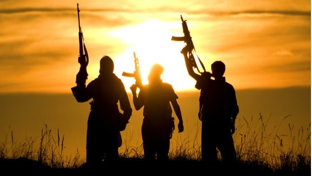 Soldiers standing against a sunset with their guns held in the air.