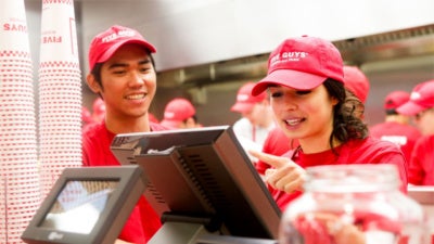Two Five Guys employees work at the cash register