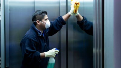 Hispanic man in a face mask cleaning the inside of an elevator