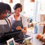 Photo of two smiling women working behind the counter of a delicatessen