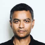 Deb Roy's headshot. A person with short hair wearing a collared shirt is positioned in front of a wall looking at the camera.