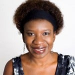 Black woman with curly hair smiling in blue and white top and a black headband.
