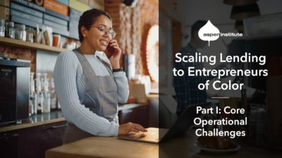 Foreground: “Scaling Lending to Entrepreneurs of Color: Part I - Core Operational Challenges.” Background: Photo of a woman of color wearing an apron and glasses behind the counter of a cafe. She is using a laptop while taking an order on her cell phone.