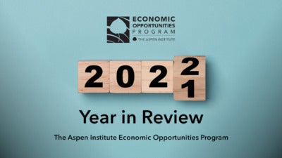 Foreground: "2021 Year in Review - The Aspen Institute Economic Opportunities Program." Background: Photo of wooden blocks spelling out the year. The final block is in the process of flipping from 2021 to 2022.