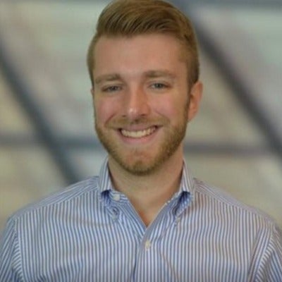 A person with short hair wearing a collared shirt smiles at the camera.