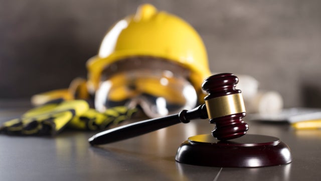 Photo of a gavel with a hard hat, safety googles, and work gloves in the background.