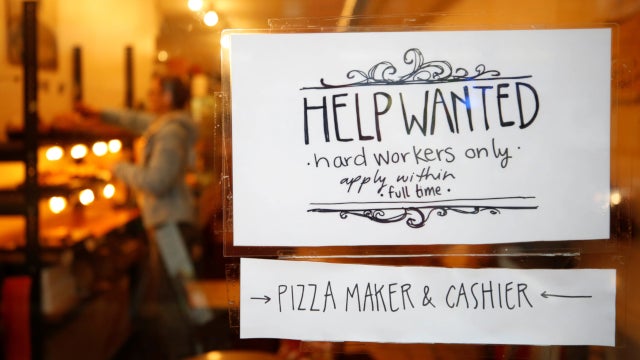 Photo of a help wanted sign in the window of a pizza shop