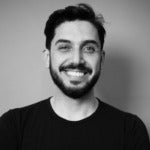 Eric Asmar's headshot. Image depicts a person with short hair, a mustache, and beard wearing a t-shirt smiling at the camera.
