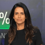 Jag Gill's headshot. A person with long hair wearing a t-shirt is in front of a sign looking at the camera.
