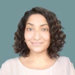 Doctor Karima Ladhani's headshot. Image depicts a woman with curly, shoulder-length hair wearing a blouse smiling at the camera.