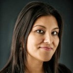 S. Mitra Kalita's headshot. A person with medium-length hair is positioned in front of a dark background looking at the camera.