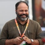 C.C. Joseph's headshot. A person with short hair and a beard wearing a headset, lanyard, and collard shirt holds a remote control and smiles.