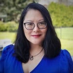 Poesy Chen's headshot. A person with medium-length hair wearing a blouse, glasses, and a necklace is positioned outside on a patio deck, looking at the camera.