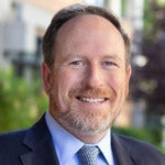 White man in a suit and tie smiles and looks into the camera