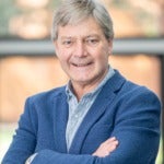 Headshot of man in blue blazer and gray hair smiling at camera