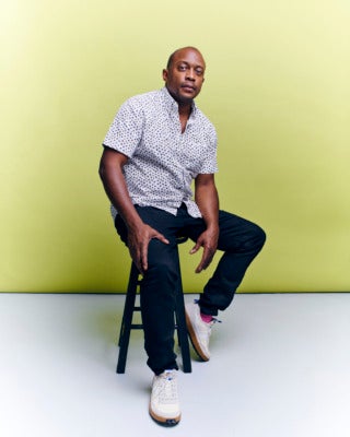 Photo of artist Hank Willis Thomas sitting on a stool in front of a yellow background.
