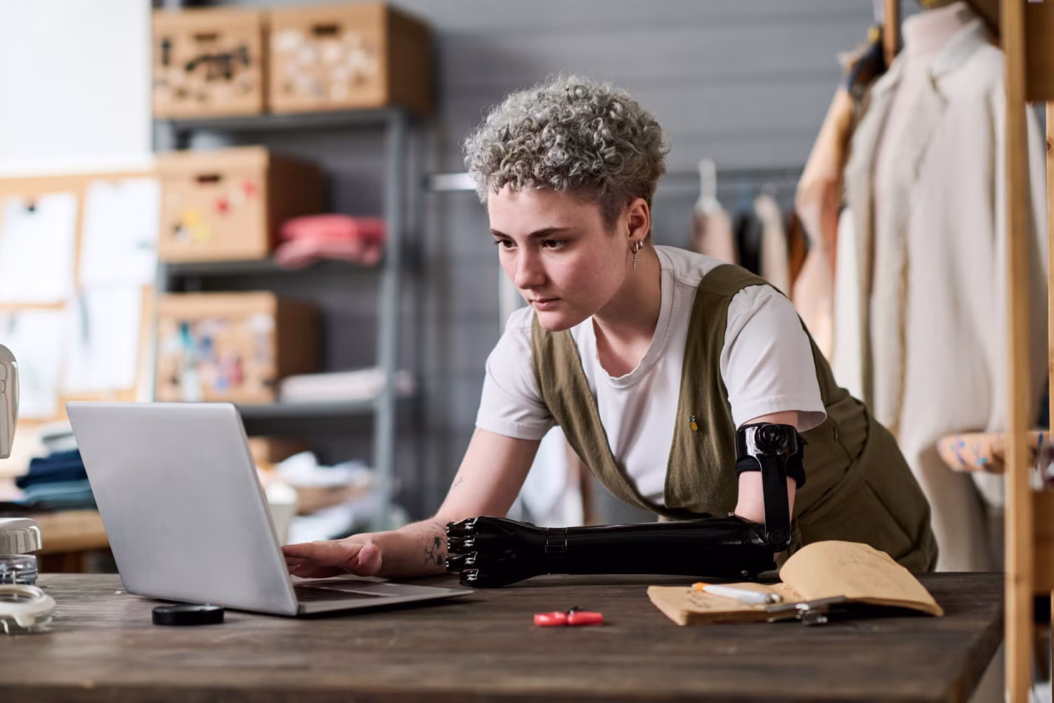 A photograph of a young fashion designer with a prosthetic arm using a laptop.