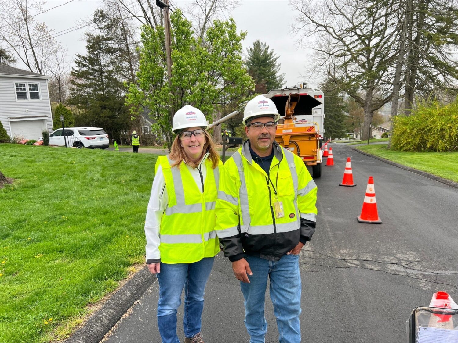 Photo of Leslie Kass and a Lewis Tree Services Employee. They are standing on a road, both wearing hard hats and reflector vests.