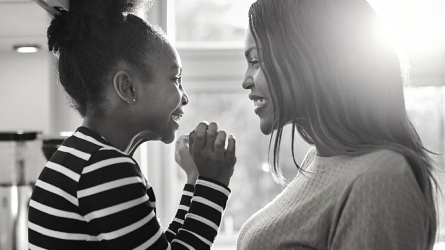 Black mother and young daughter facing each other and smiling.