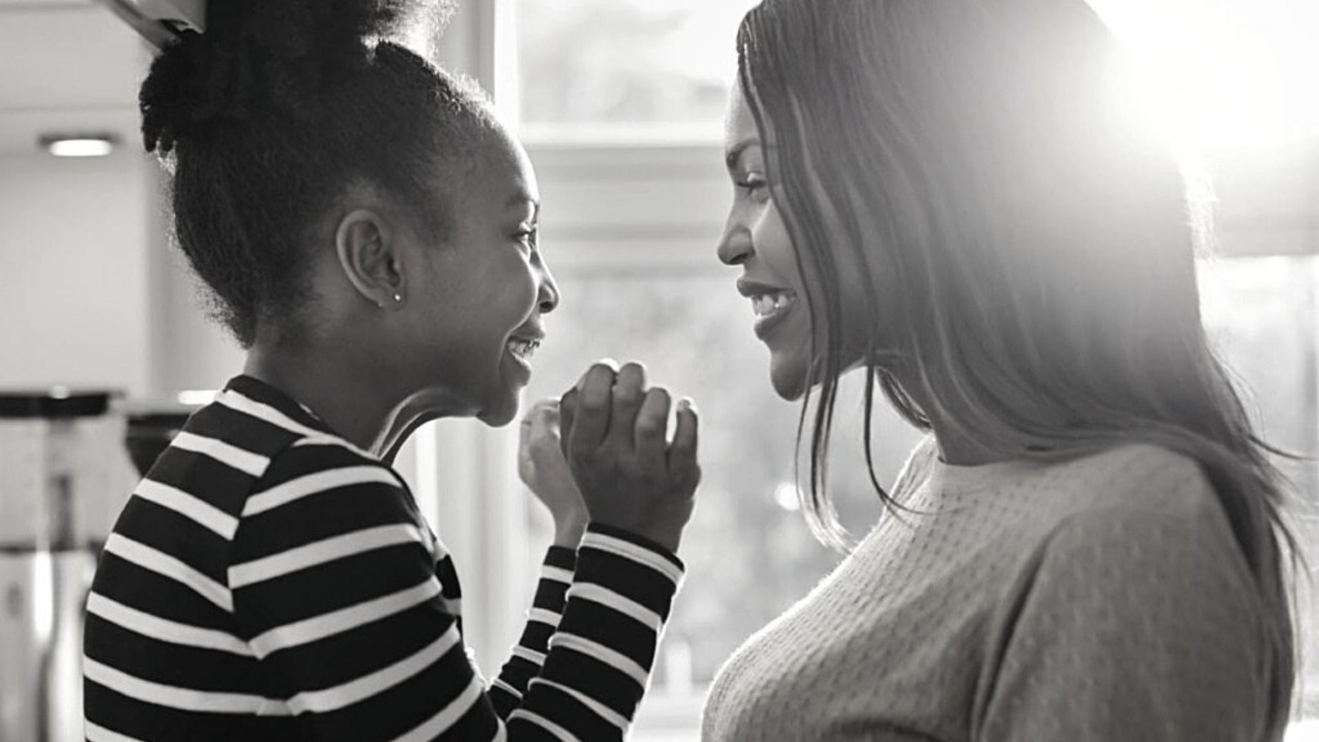 Black mother and young daughter facing each other and smiling.
