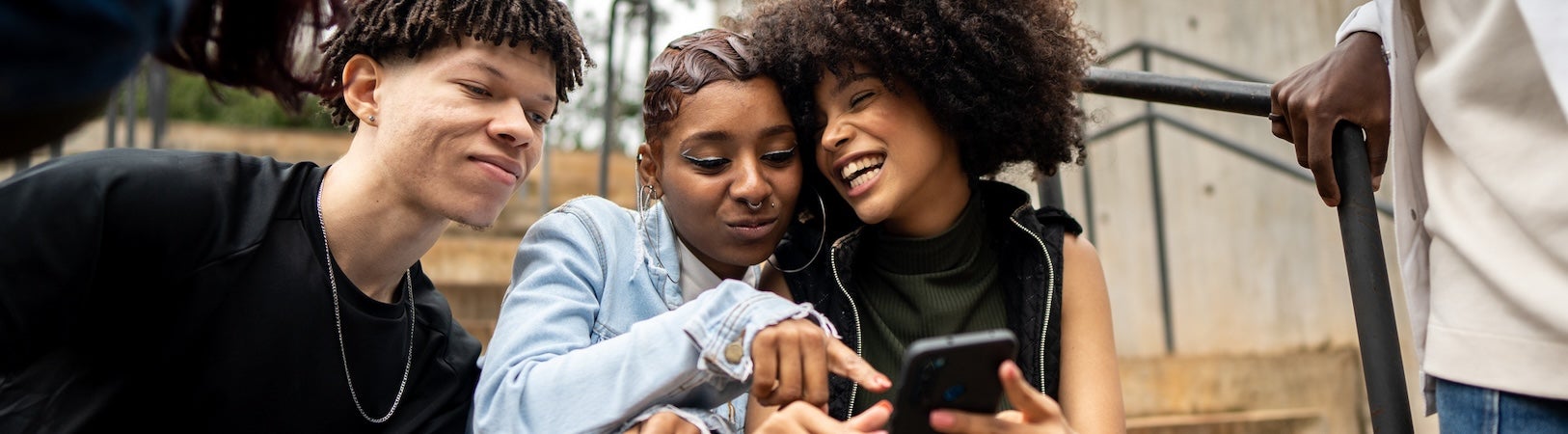 A group of teenagers gathered on a staircase look at a phone screen, representing digital wellbeing among youth.