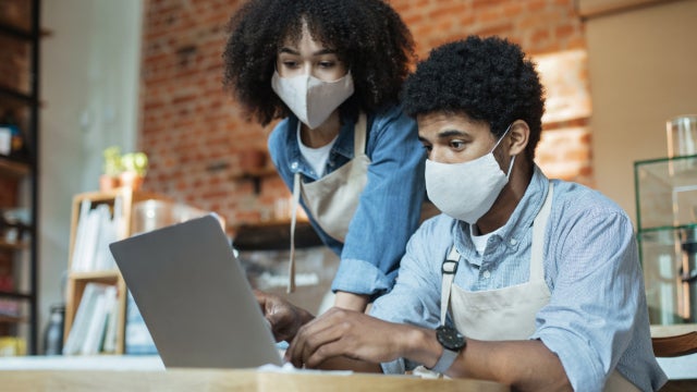 Photo of two small business owners wearing face masks while working at a laptop