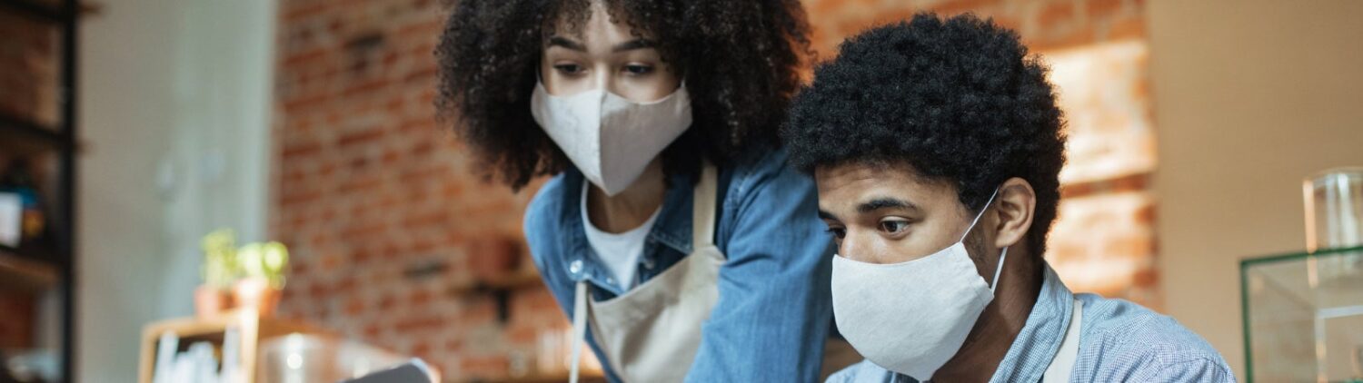 Photo of two small business owners wearing face masks while working at a laptop
