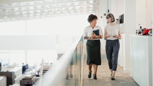 Photo: Two women converse with each other while walking through an office
