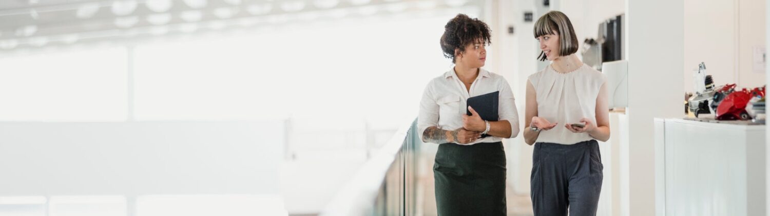 Photo: Two women converse with each other while walking through an office