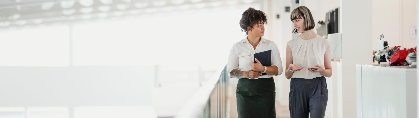Photo: Two women converse with each other while walking through an office