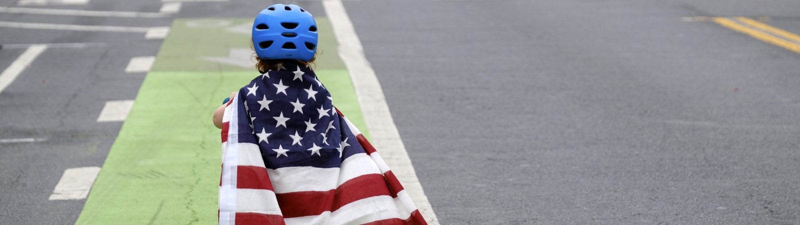 Child on a scooter wearing an American flag as a cape