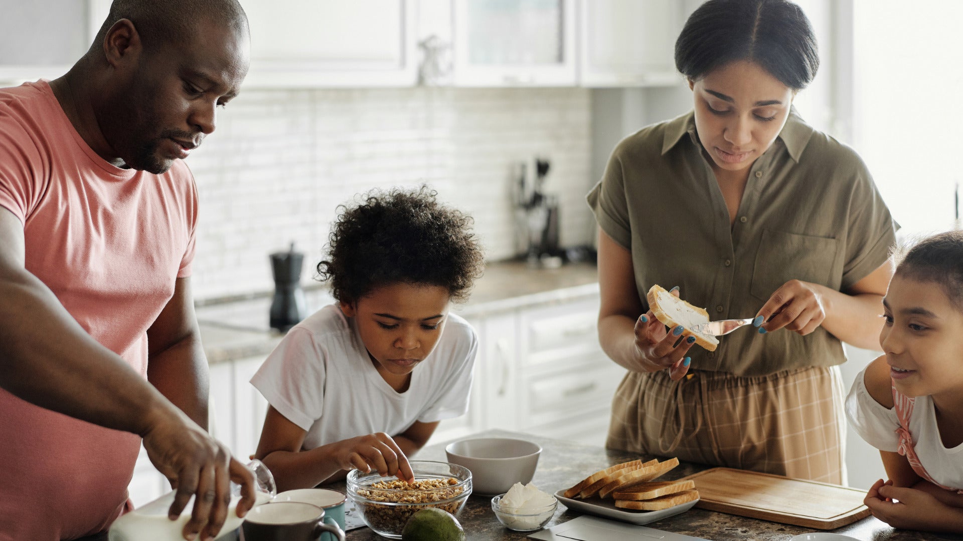 Black family of four make food around a kitchen island.