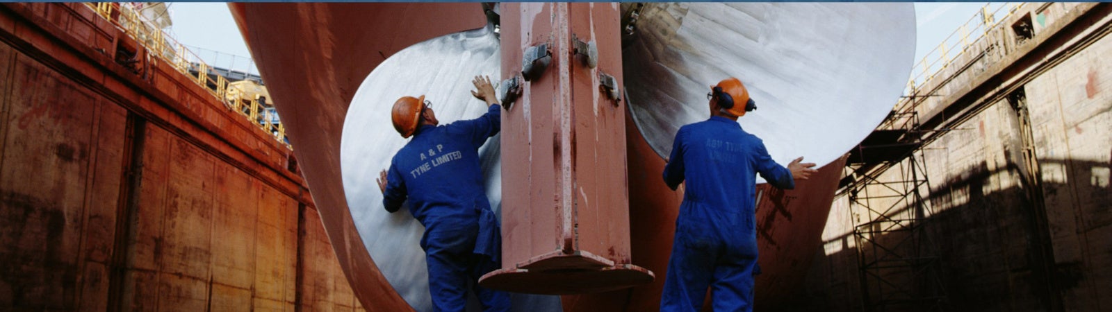 Two men working on the propeller of a ship, on a dry dock