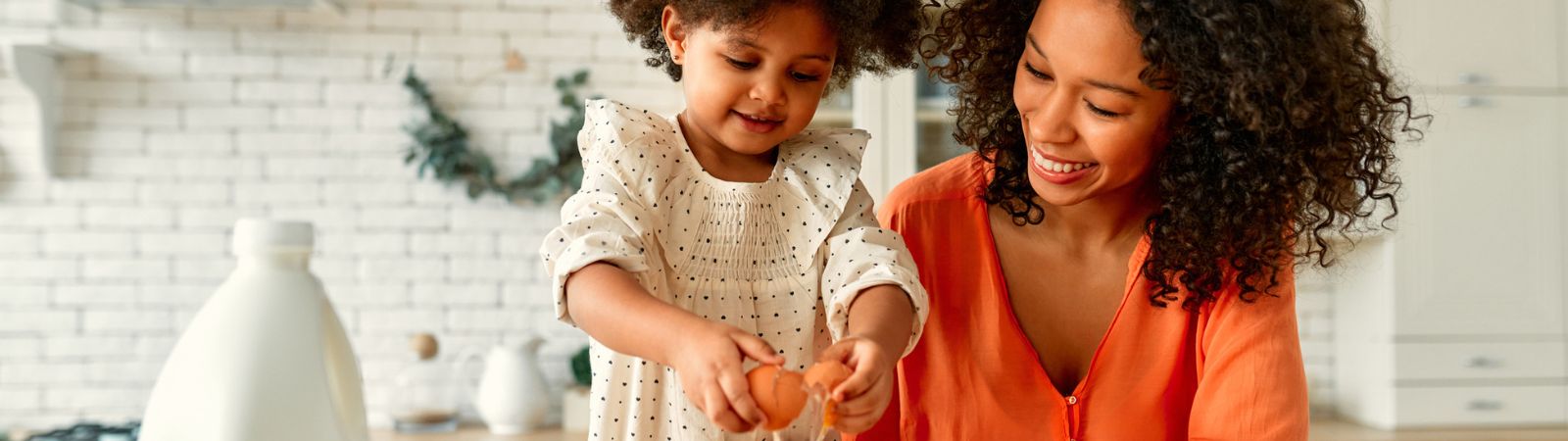 Mother and daughter baking. Little girl cracks an egg.