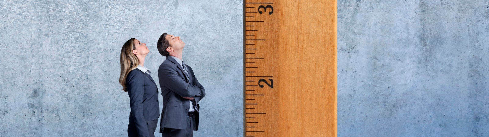 Man and woman in professional attire staring upward at a giant ruler