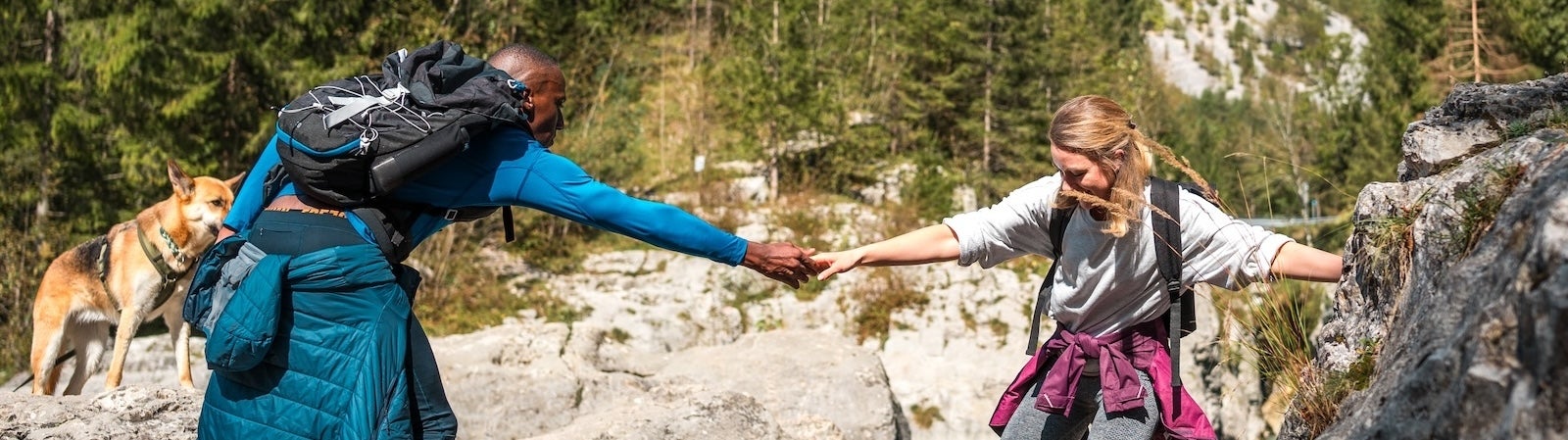 A person in hiking gear helps another person in hiking gear cross a river, representing trust-building in tech.