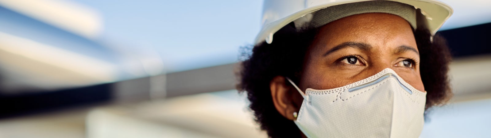 Black woman worker wearing a hard hat, reflector vest, and face mask.