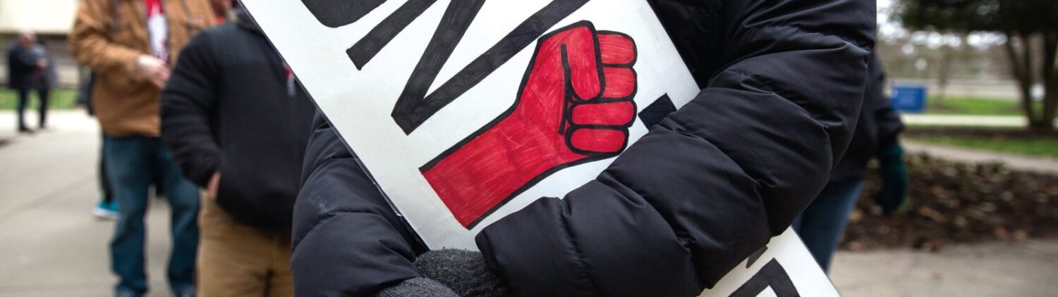 Union worker holds a sign that says "UNITED" with a raised fist symbol in place of the "I"