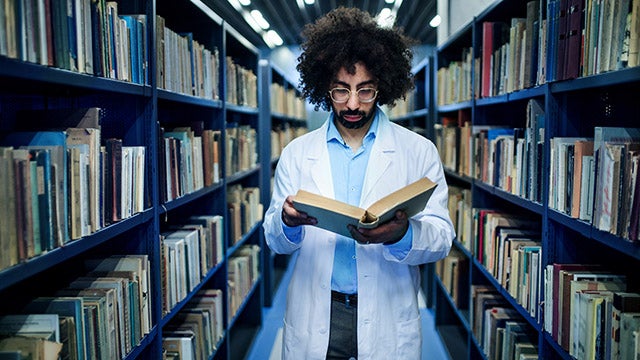 Doctor standing in library, studying information about corona virus.