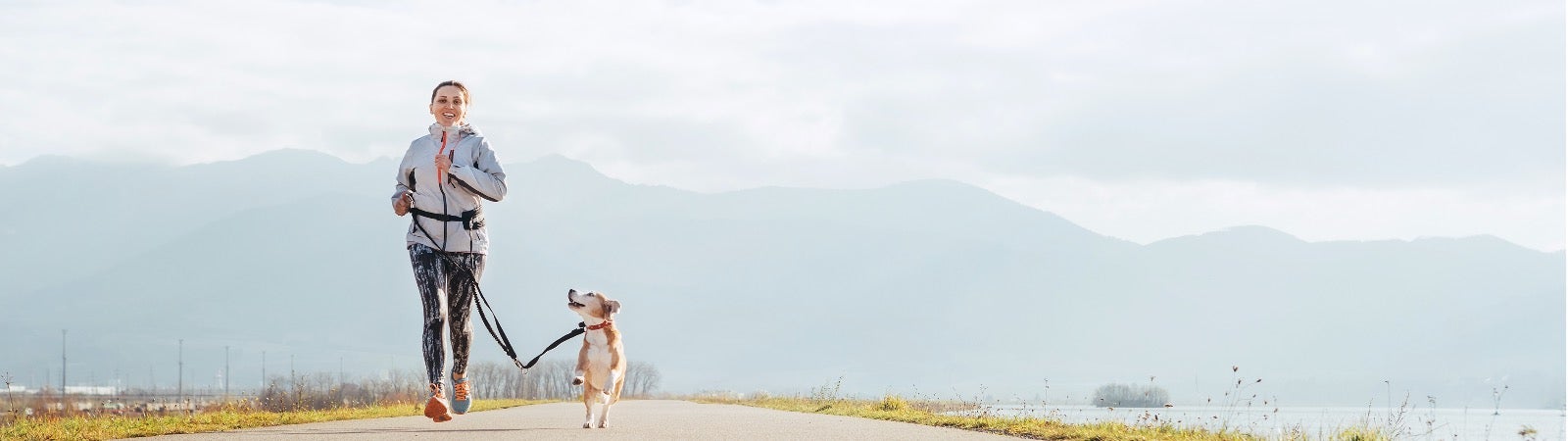 A woman running outside on a road with her dog.