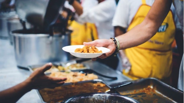 A volunteer hands a plate of food to someone in line at a soup kitchen.