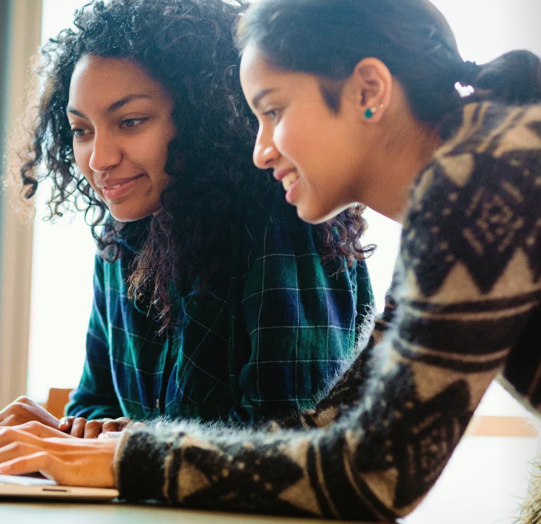 Two teenagers work together on a laptop computer.