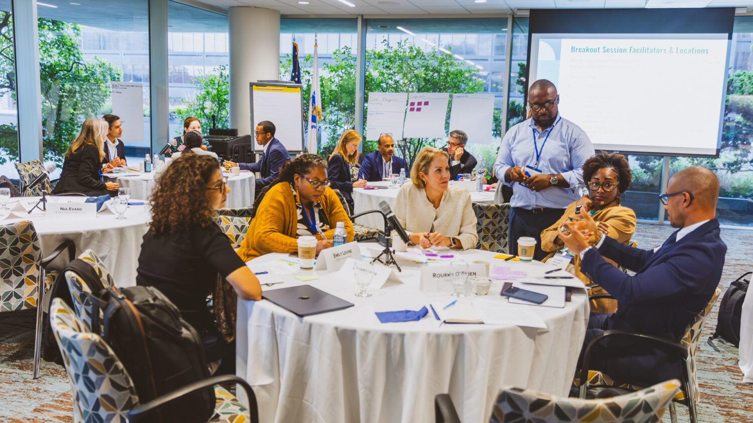 Participants at the September 2025 Essential Wealth convening are shown seated at round tables in discussion.