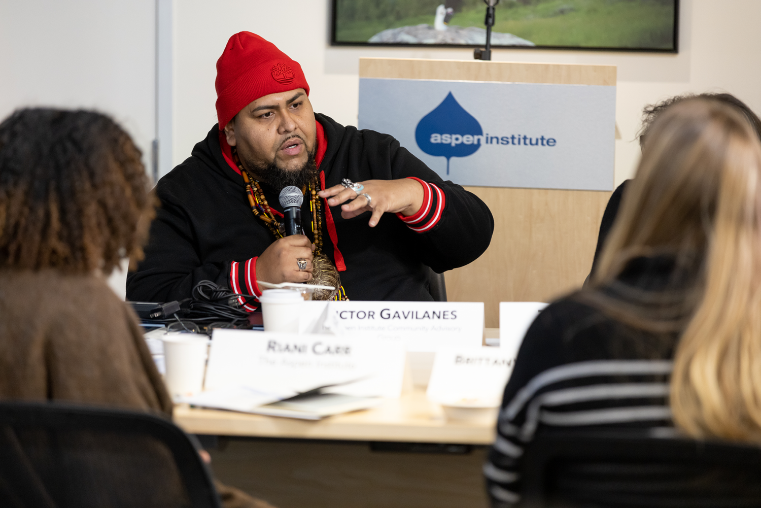 A man speaks into a microphone at a table of event participants.