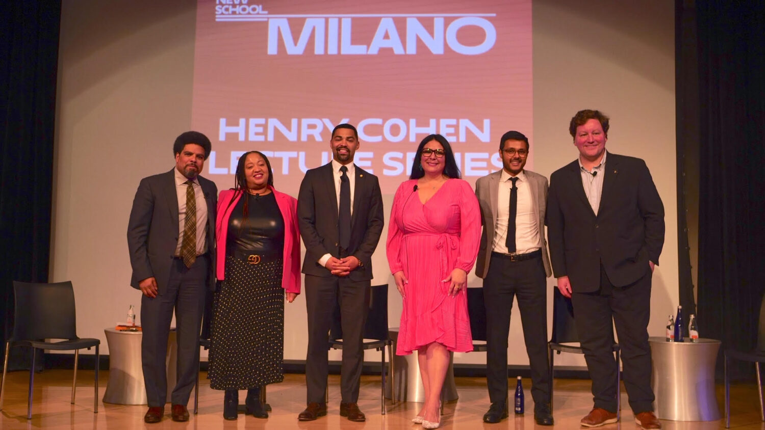 Six people stand on a stage before a banner saying "The Henry Cohen Lecture Series."