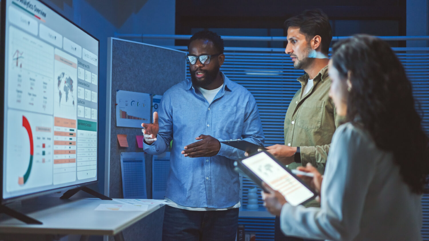 3 tech workers look at a large screen with data on it